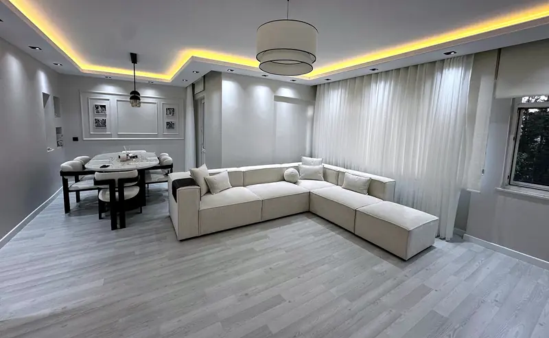 Gri salonda krem L koltuk ve yemek masası